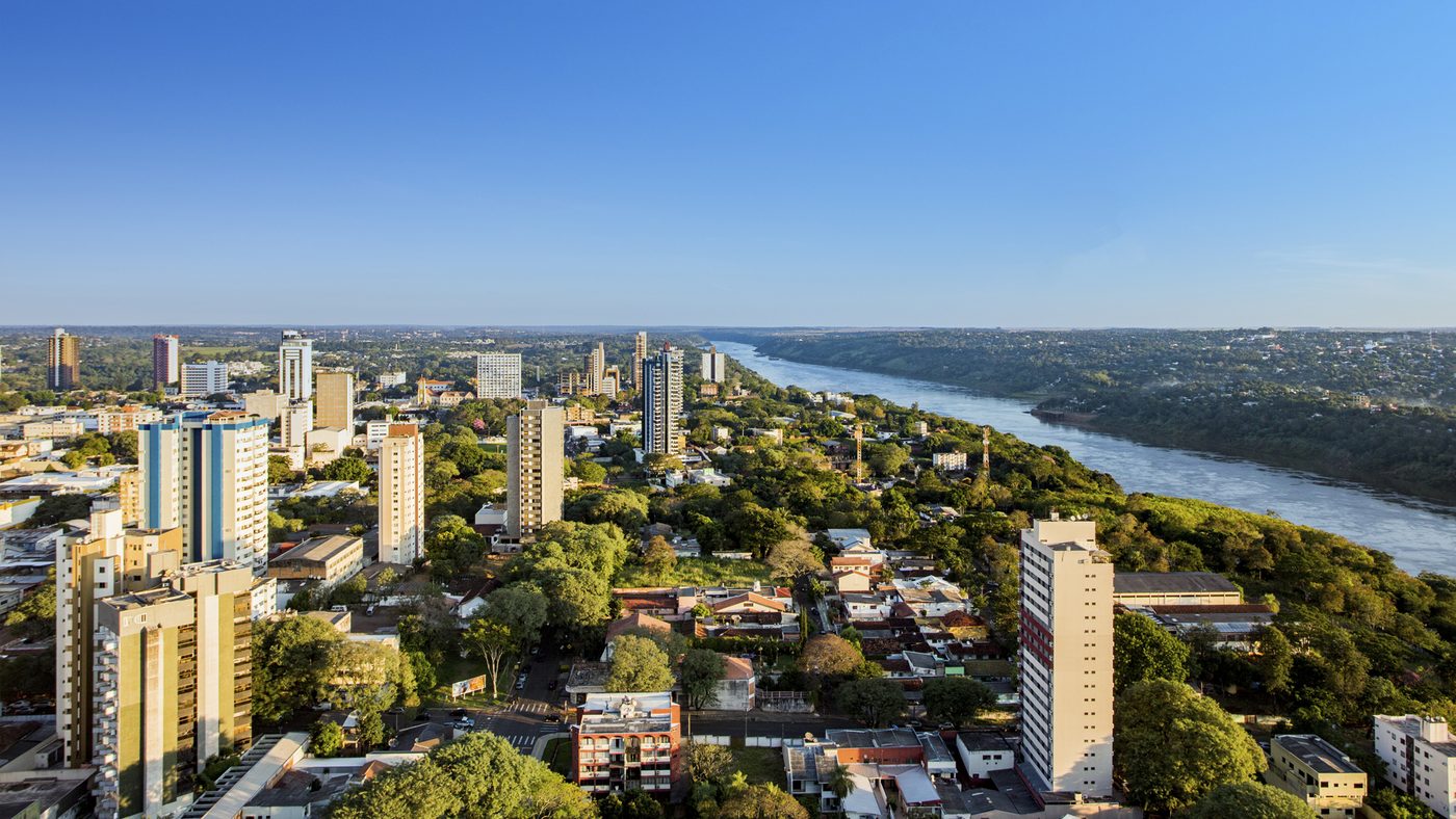 Vista aérea de Foz do Iguaçu, com prédios, áreas verdes e um rio ao fundo