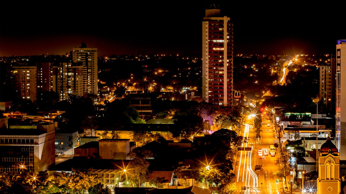 Avenida movimentada de Foz do Iguaçu à noite, com prédios iluminados